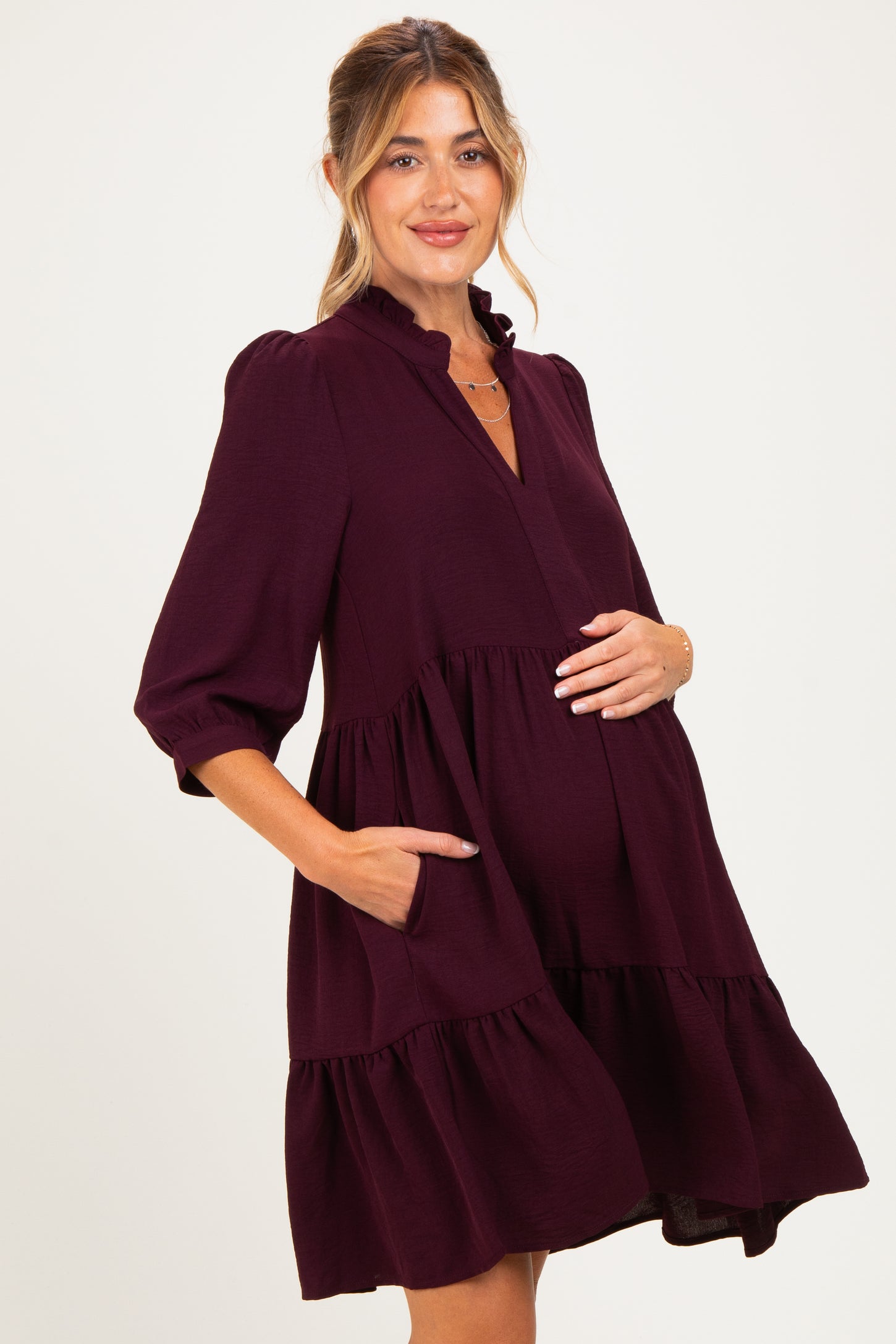 woman wearing a dark burgundy maternity dress with short puff sleeves and pockets, showing her baby bump