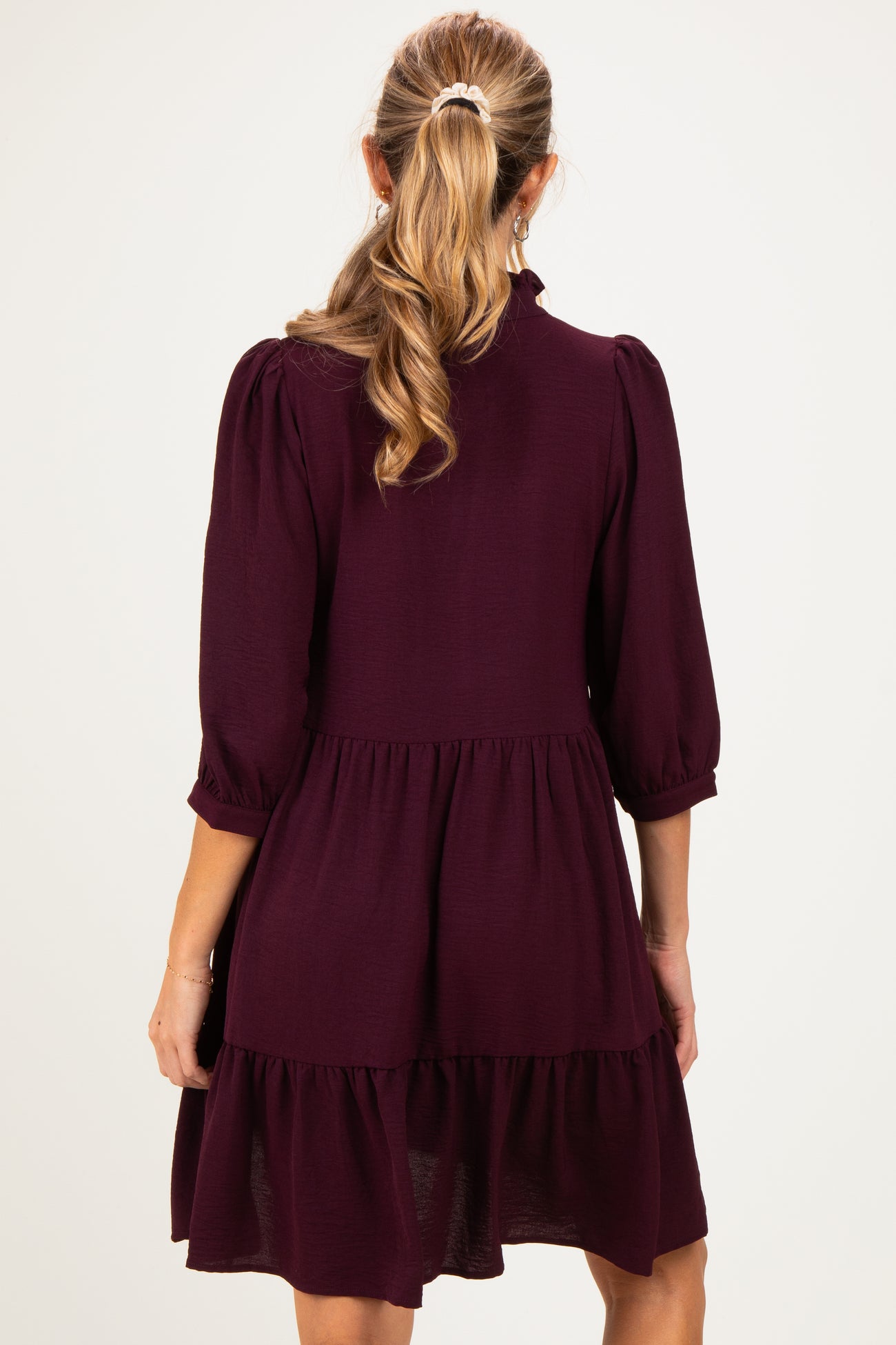 woman wearing a burgundy maternity dress with three-quarter puff sleeves and a tiered skirt, seen from the back