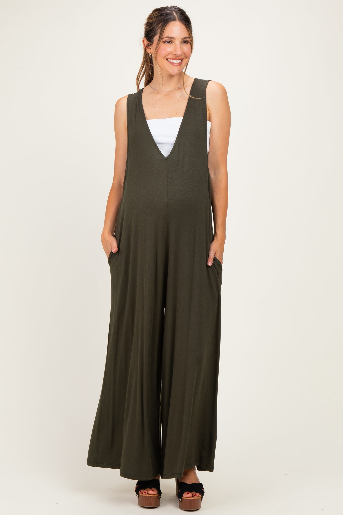woman wearing an olive green maternity jumpsuit with a deep v-neck and pockets, showing her baby bump