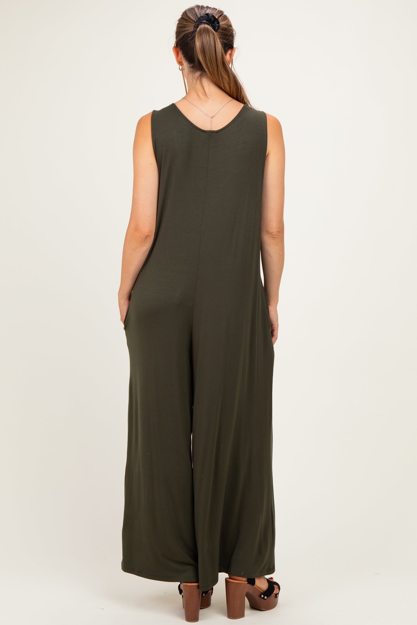 woman wearing an olive green maternity jumpsuit with a loose fit and wide legs, viewed from the back
