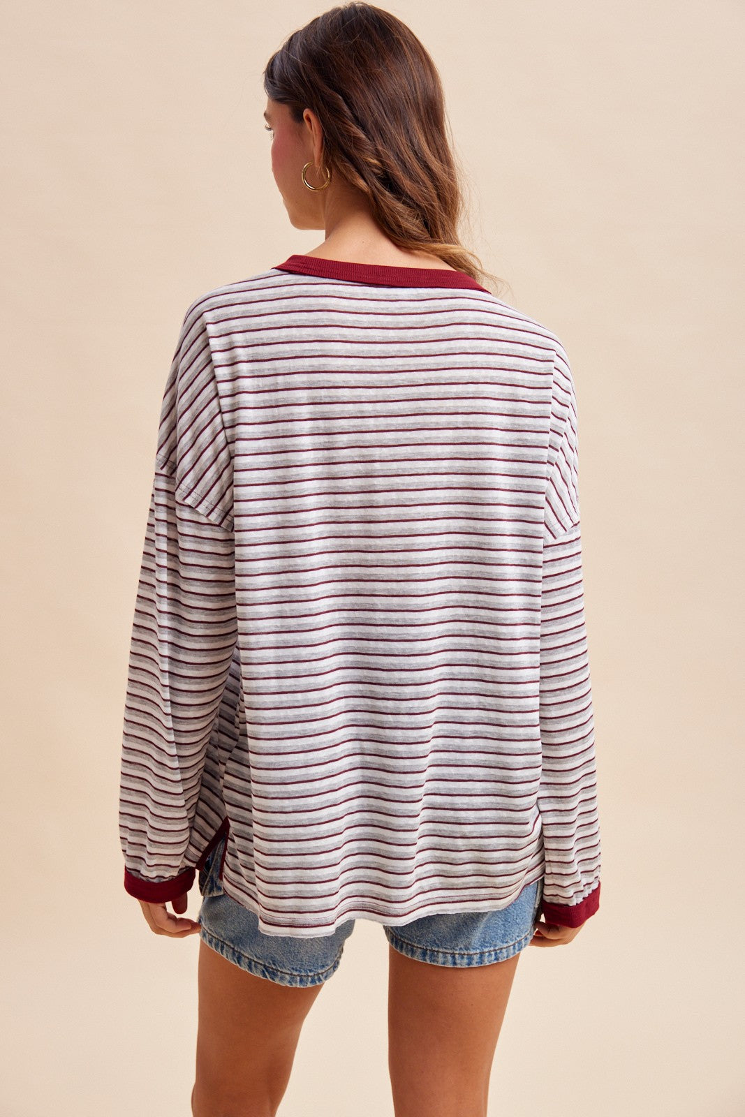 woman wearing a burgundy and cream striped long sleeve top with a relaxed fit and paired with denim shorts