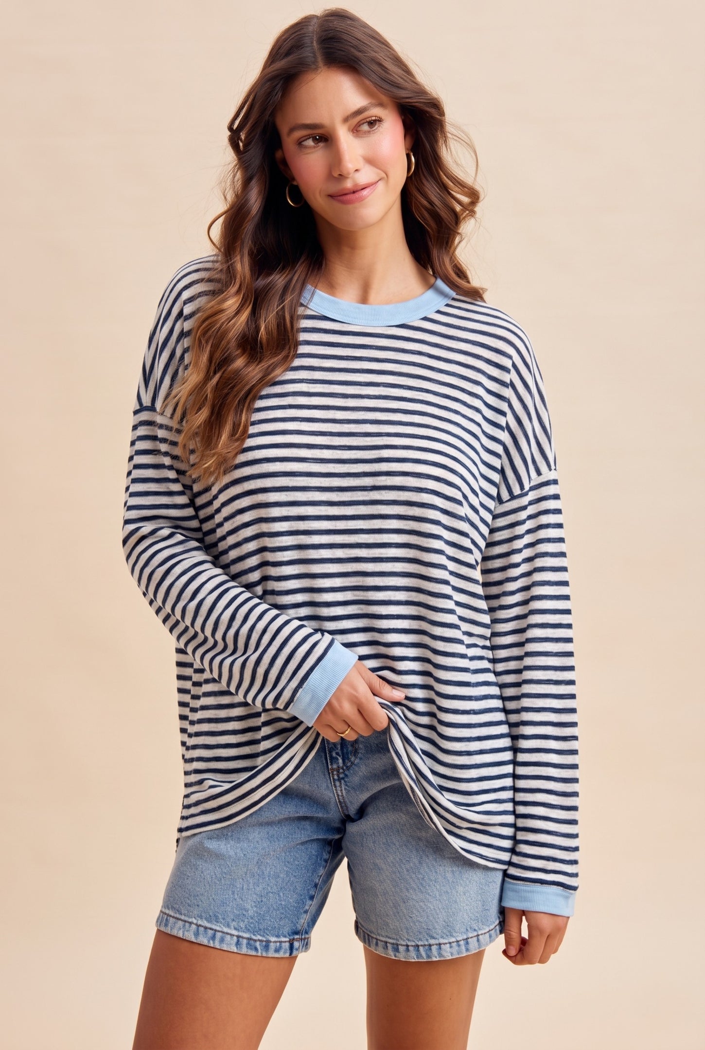 woman wearing a striped oversized long sleeve top with light blue accents and denim shorts