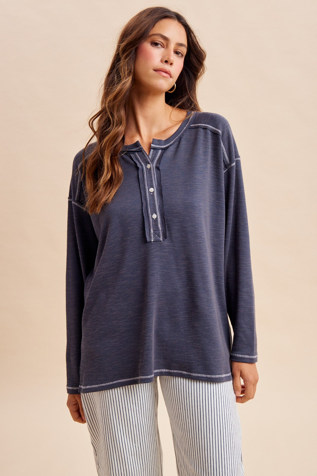woman wearing a dark gray long sleeve henley top with button closure and contrasting stitching, styled with striped pants