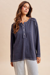 woman wearing a dark gray long sleeve henley top with button closure and contrasting stitching, styled with striped pants