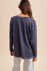 woman wearing a dark gray long sleeve oversized top with a crew neckline and ribbed texture, viewed from the back