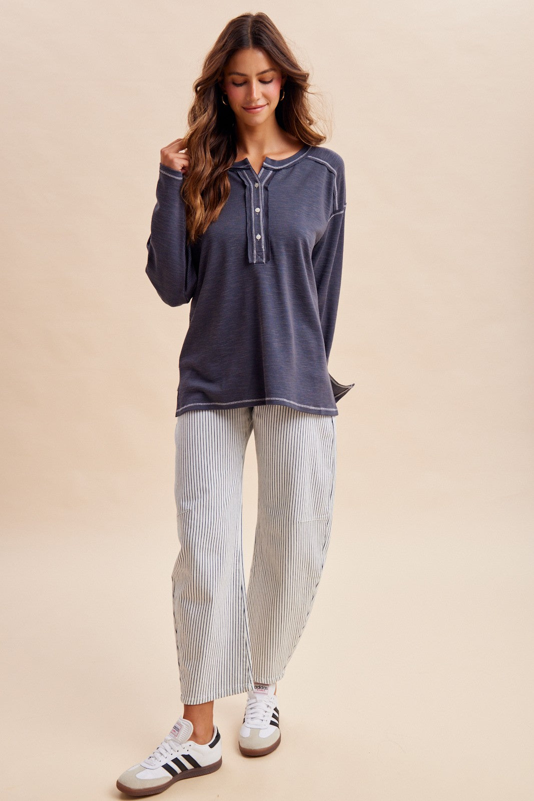 woman wearing a navy blue long sleeve henley top and white striped wide-leg pants with sneakers