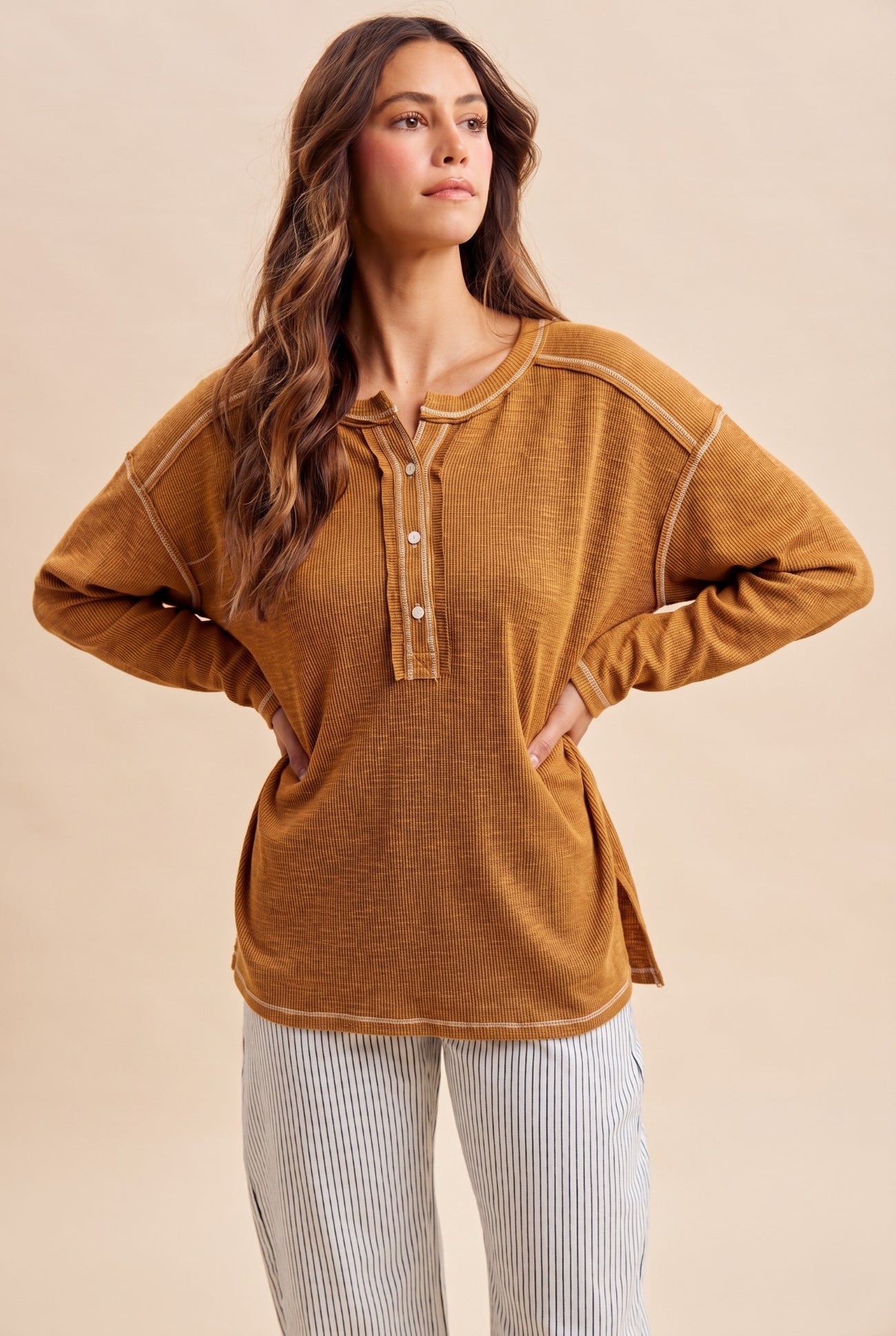 woman wearing a mustard yellow long sleeve henley shirt with button details and side slits, paired with striped pants