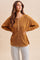 woman wearing a mustard yellow long sleeve henley shirt with button details and side slits, paired with striped pants