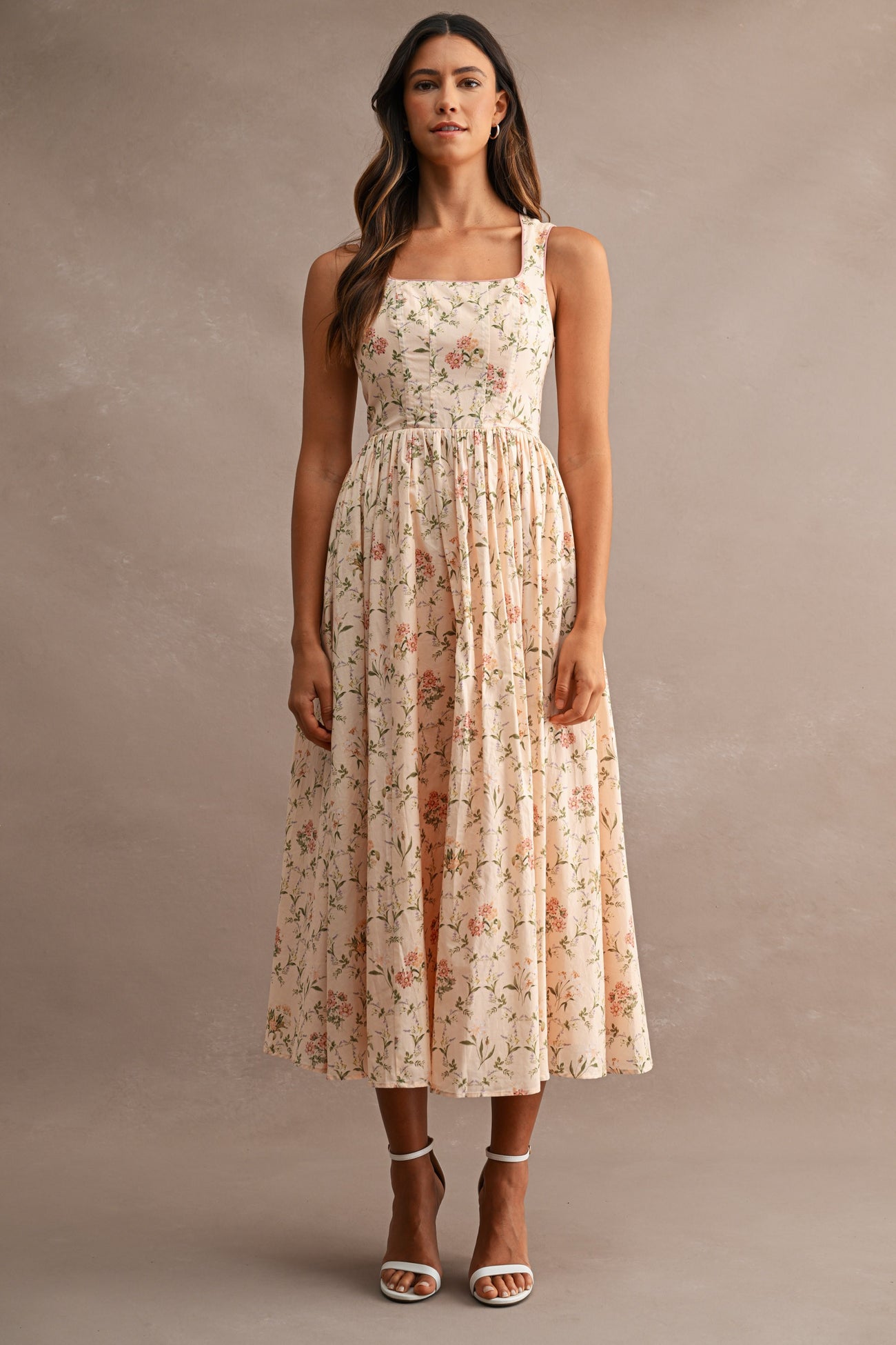woman wearing a floral midi dress with a square neckline and adjustable straps, paired with strappy heels