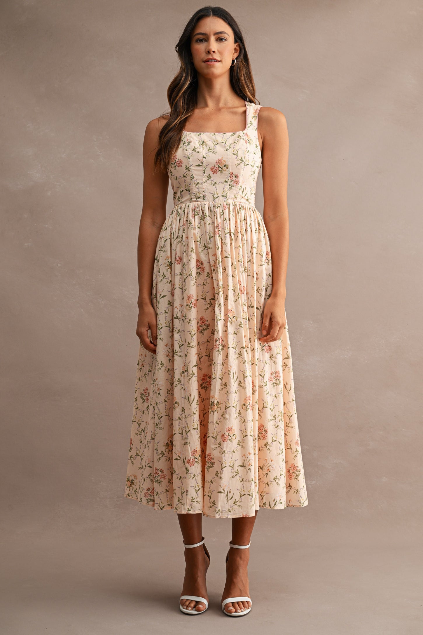 woman wearing a floral midi dress with a square neckline and adjustable straps, paired with strappy heels