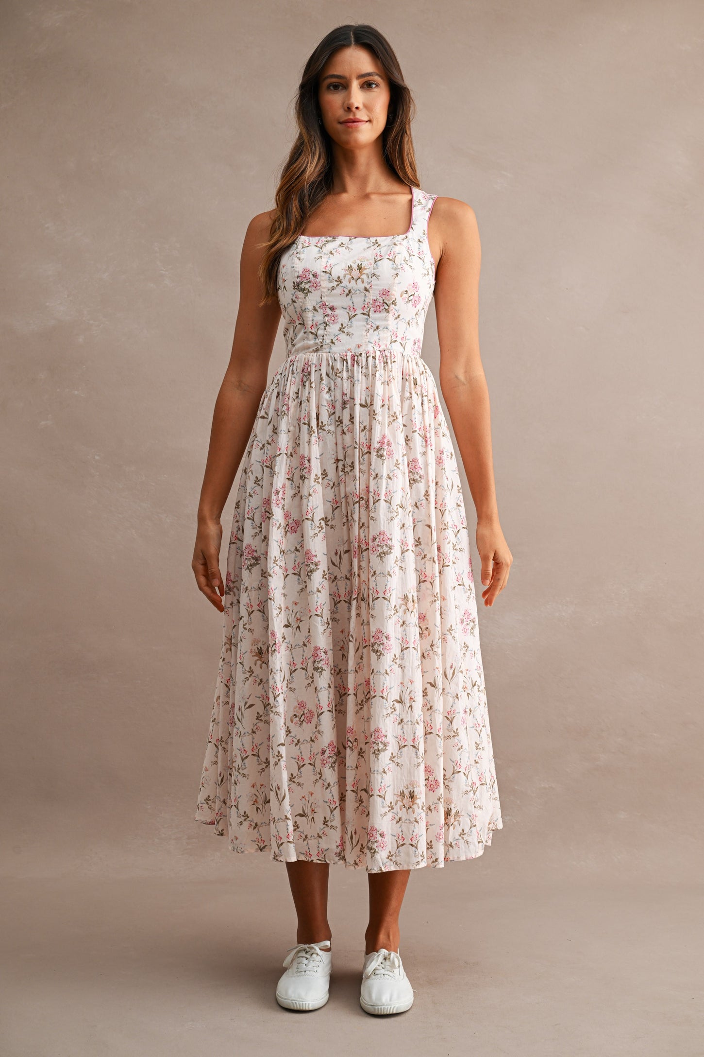 woman wearing a floral print midi dress with a square neckline and a flowy skirt, paired with white sneakers