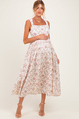 woman wearing a floral maternity dress with a square neckline and a flowing skirt, gently holding her baby bump