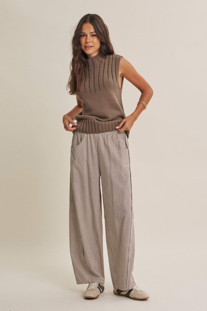 woman wearing a sleeveless brown ribbed sweater and striped wide-leg pants, standing casually with hands in pockets