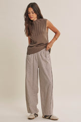 woman wearing a taupe knitted sleeveless top with ribbed details and wide-striped high-waisted trousers