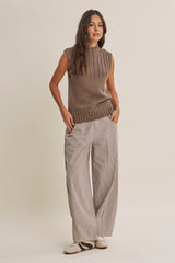 woman wearing a brown sleeveless textured sweater and striped wide-leg pants, standing with hands in pockets