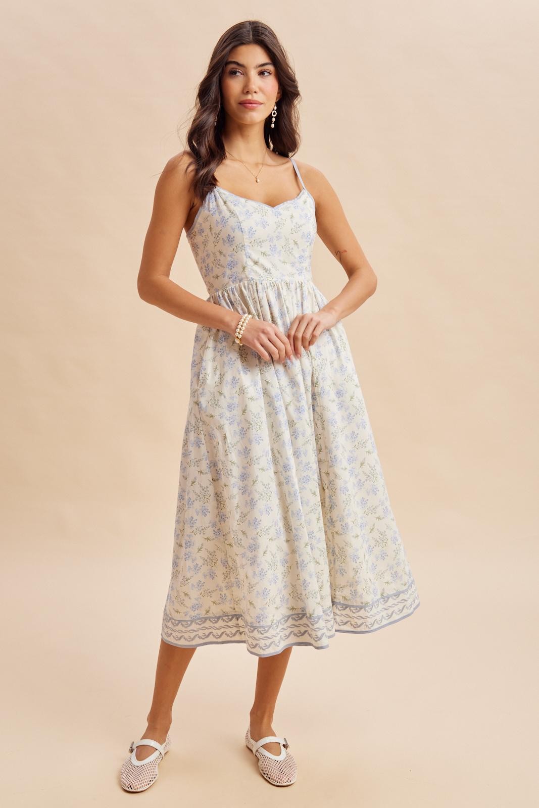woman wearing a light yellow floral midi dress with adjustable straps and a smocked waist, styled with woven flats