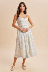 woman wearing a light yellow floral midi dress with adjustable straps and a smocked waist, styled with woven flats