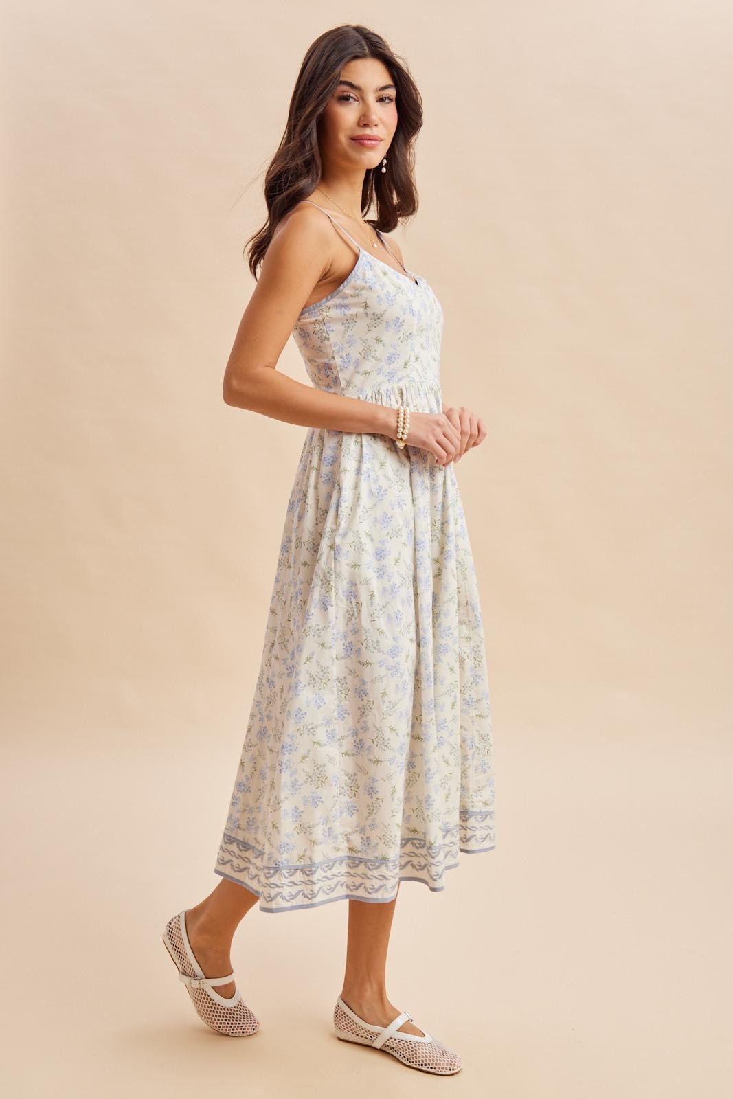 woman wearing a floral midi dress with thin straps and a cinched waist, paired with slip-on shoes