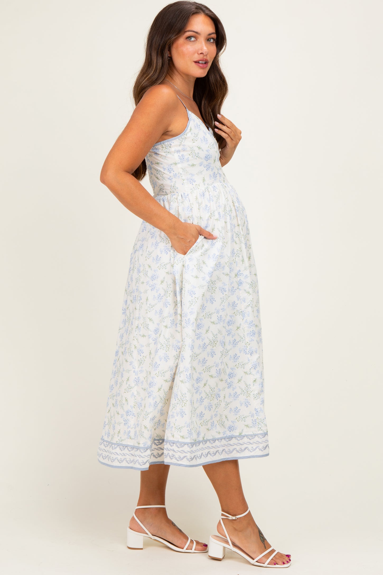 woman wearing a floral patterned maternity dress with pockets and a baby bump, styled with strappy white sandals