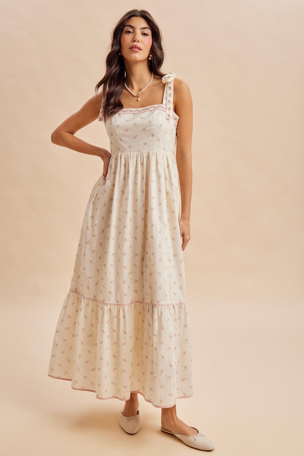 woman wearing a cream floral maxi dress with a tiered hem and a bow detail on one shoulder