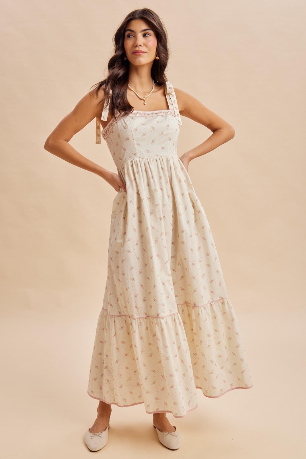 woman wearing a cream floral maxi dress with adjustable straps and a ruffled hemline