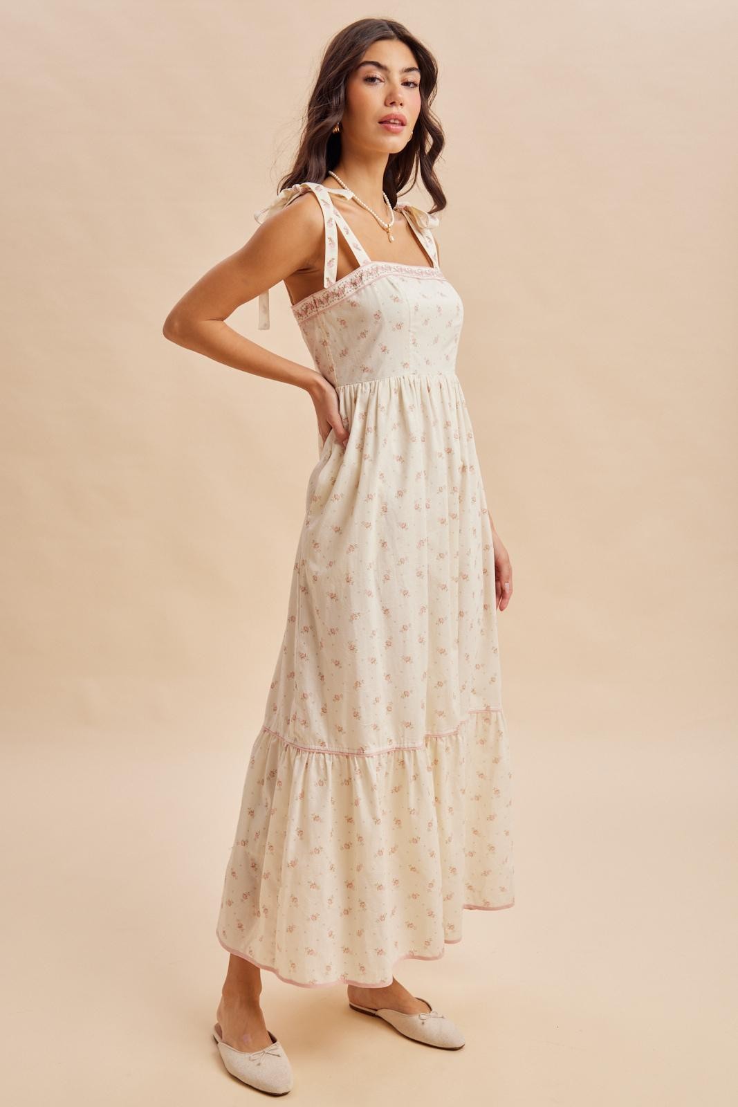 woman wearing a cream floral maxi dress with tie straps and ruffled hem, styled with slip-on shoes