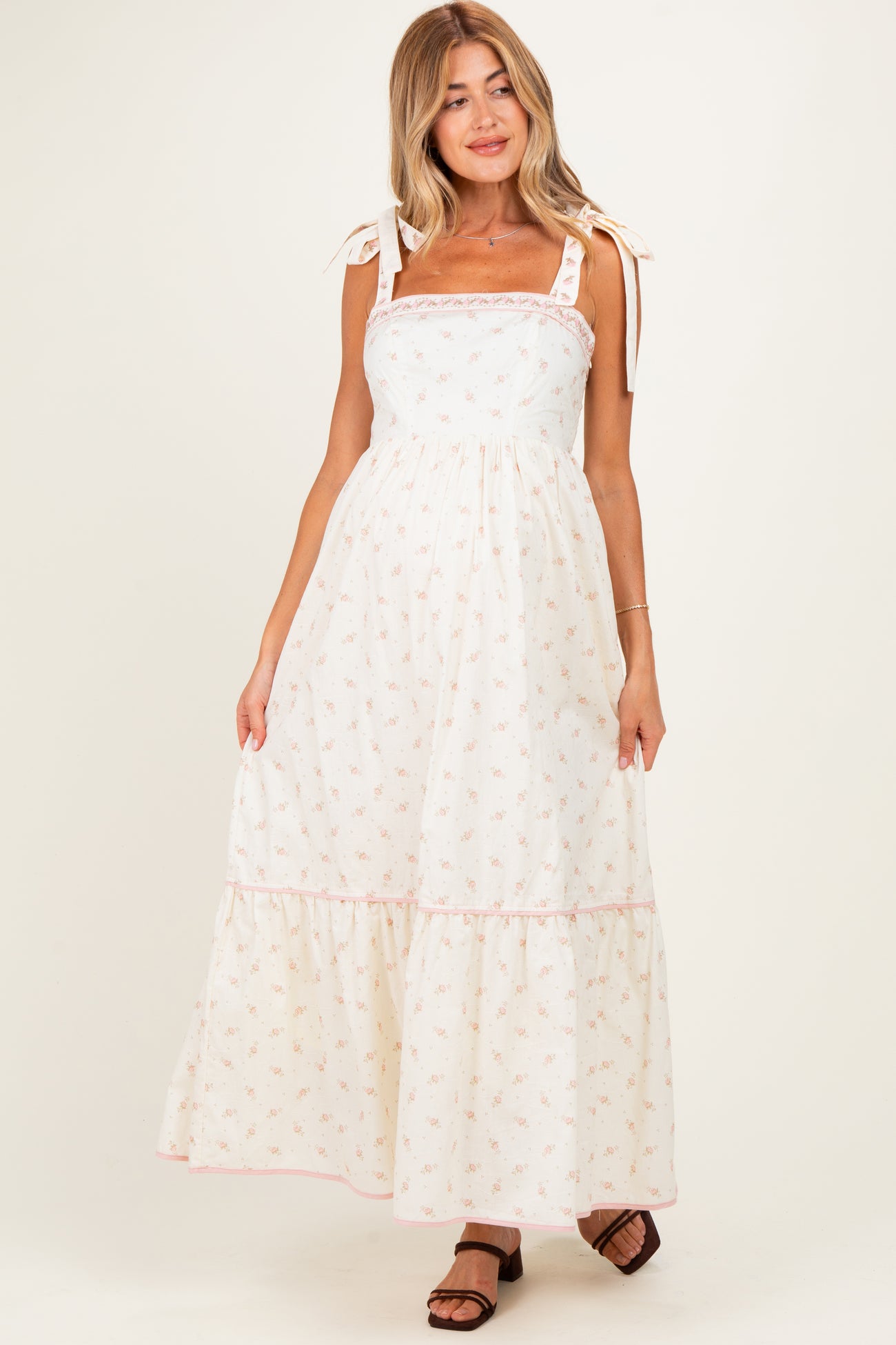 woman wearing a white floral print maternity maxi dress with tie straps and a tiered skirt, showing her baby bump