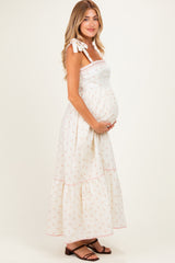 woman wearing a cream floral print maternity maxi dress with tie straps and a visible baby bump