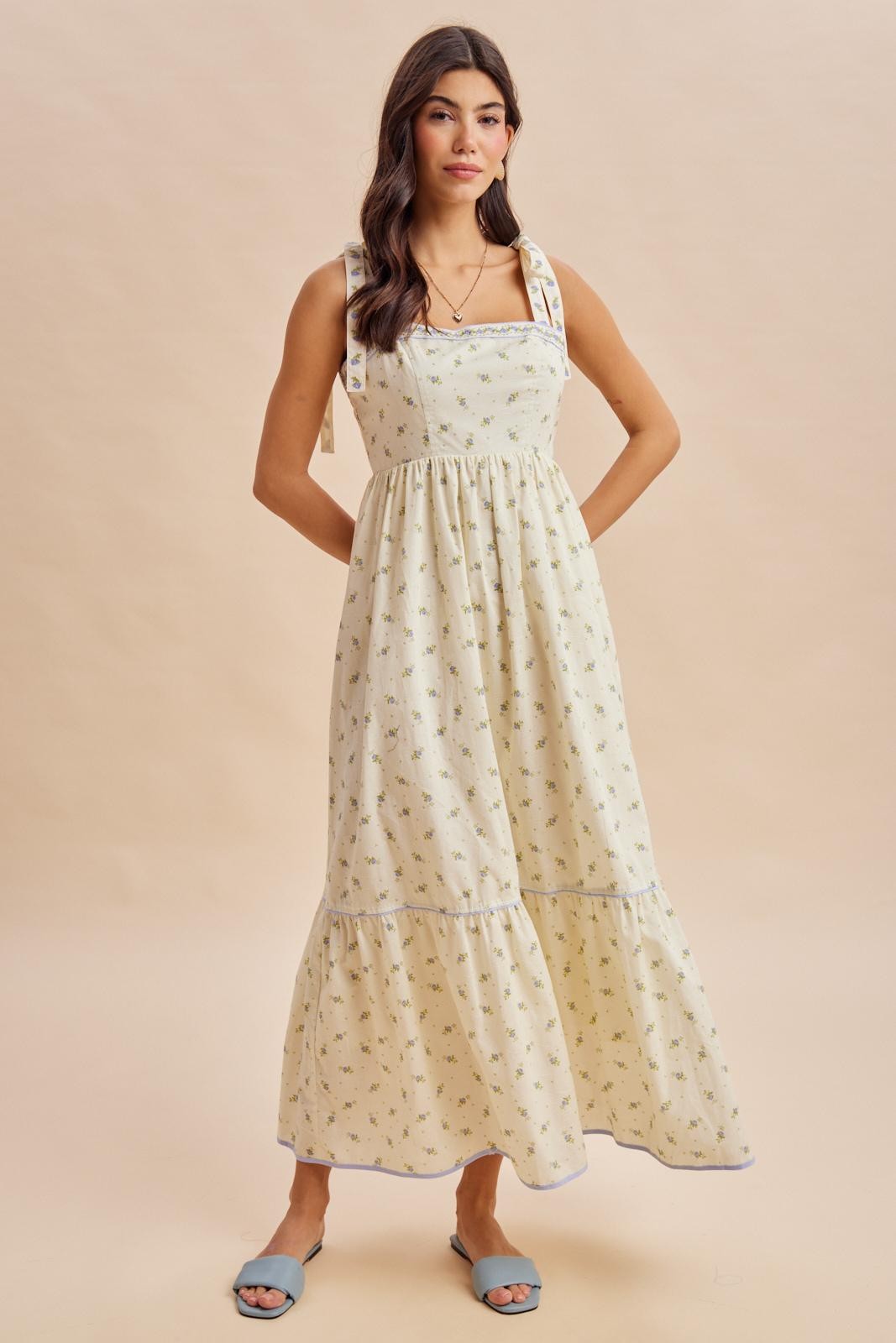 woman wearing a cream floral print maxi dress with ruffled straps and tiered skirt, styled with blue slide sandals