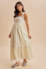 woman wearing a cream floral maxi dress with tie straps and a tiered skirt, posing against a neutral background