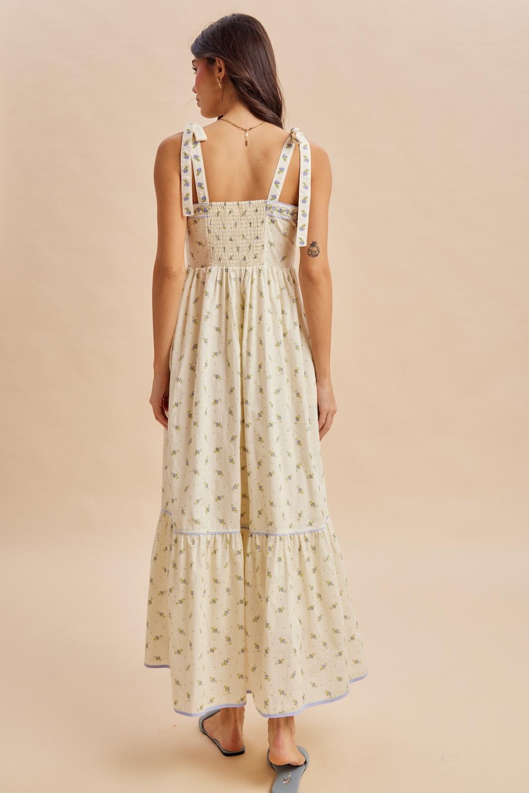 woman wearing a floral print maxi dress with smocked back and tie straps, showing a tiered hem and light neutral colors