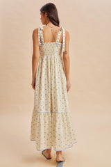 woman wearing a floral print maxi dress with smocked back and tie straps, showing a tiered hem and light neutral colors