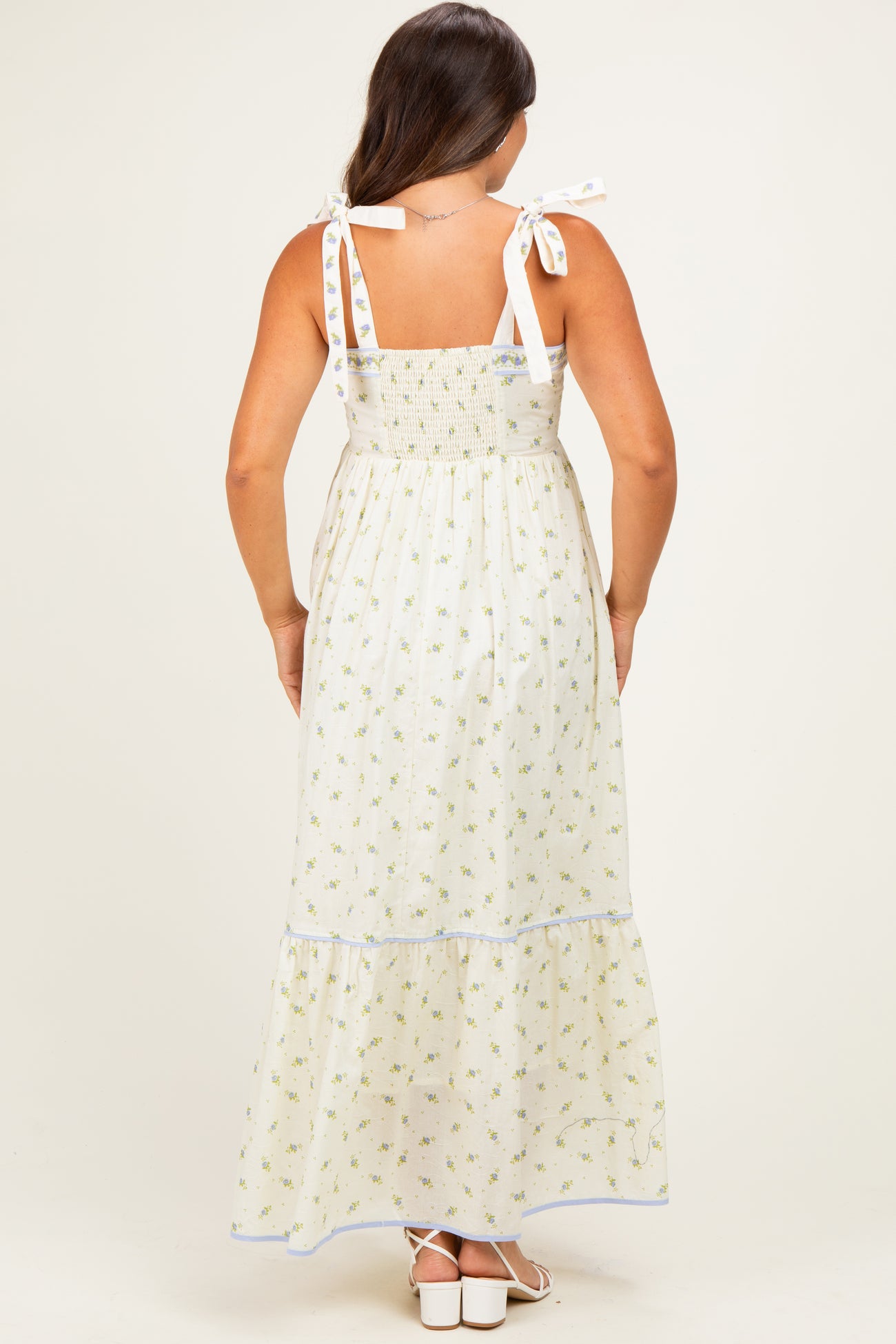woman wearing a white floral print maternity maxi dress with tie straps, showcasing a smocked bodice and tiered skirt
