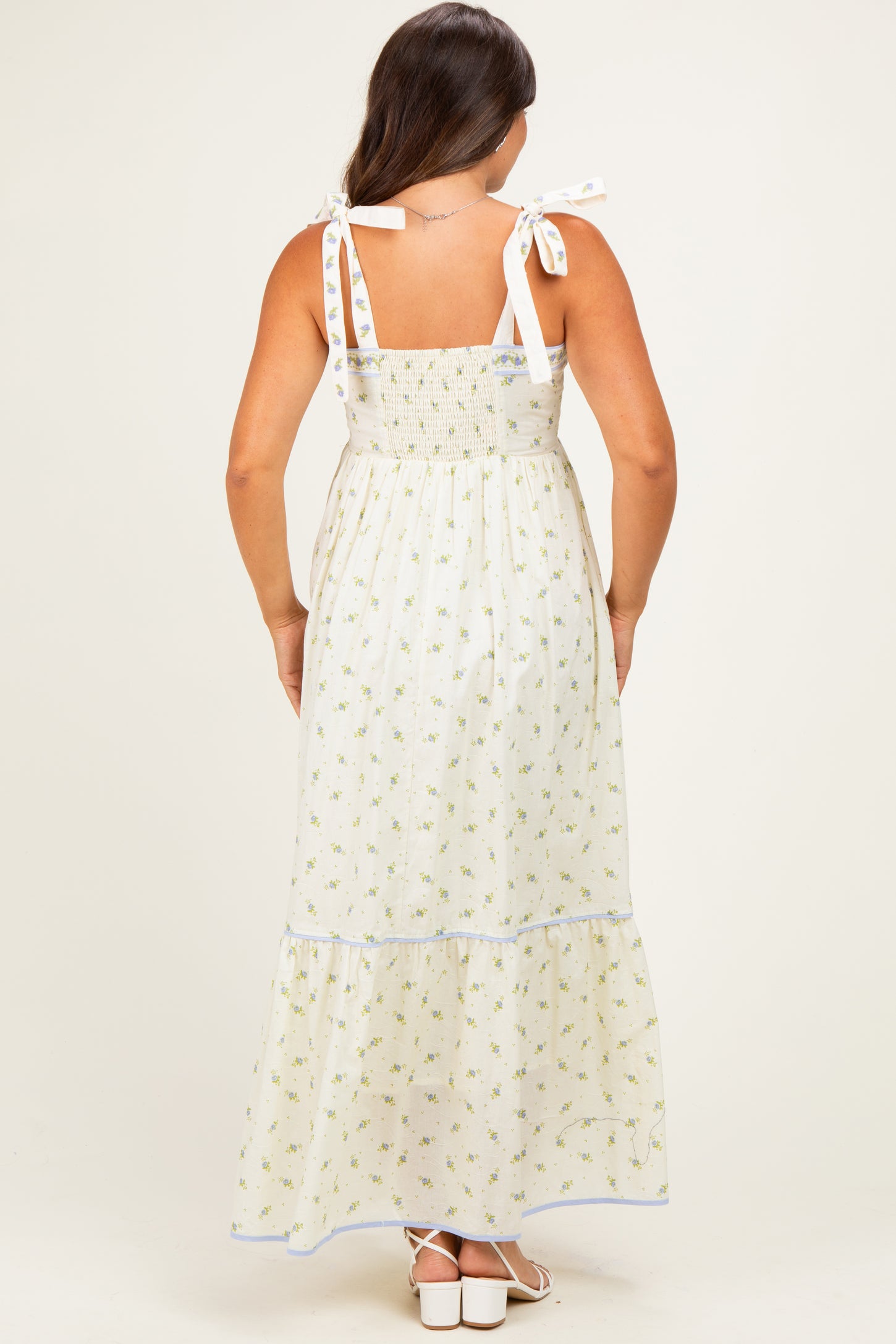 woman wearing a white floral print maternity maxi dress with tie straps, showcasing a smocked bodice and tiered skirt