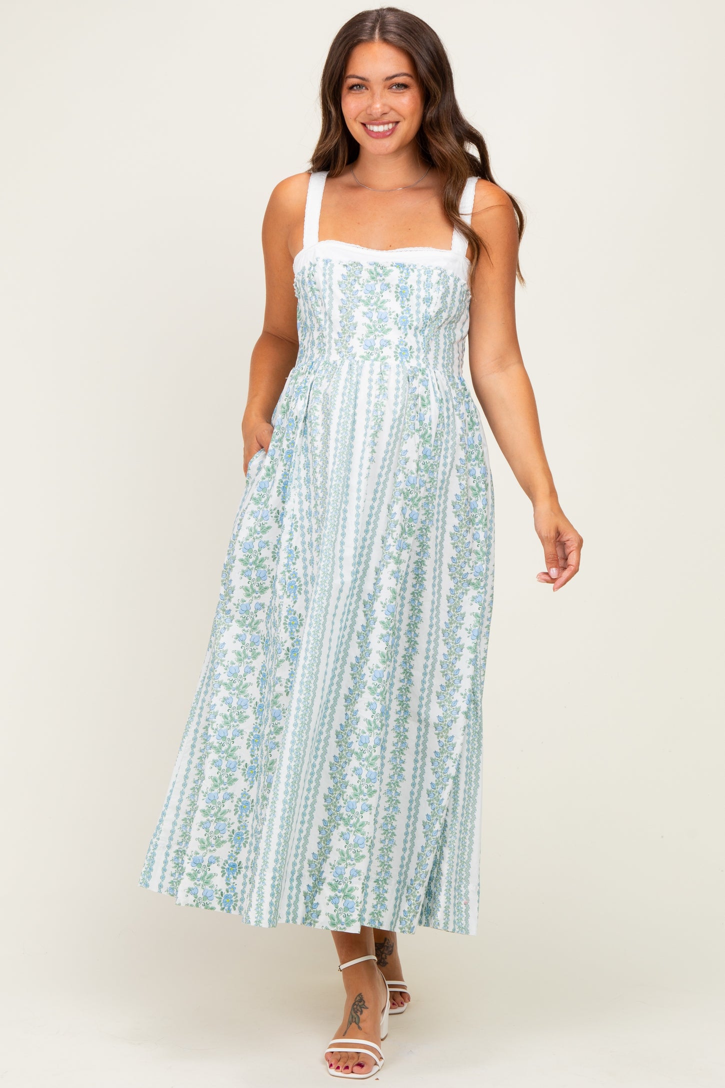 woman wearing a floral patterned maternity maxi dress with square neckline and pockets, smiling at the camera