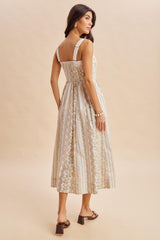 woman wearing a back view of a light beige floral maxi dress with adjustable straps and a fitted bodice