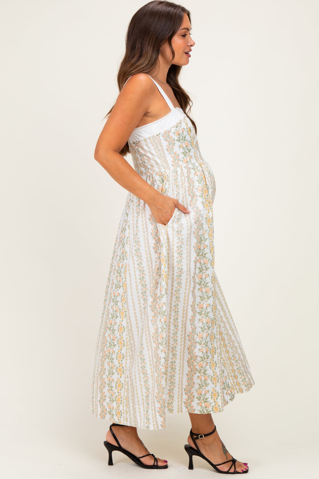 woman wearing a white floral print maternity maxi dress with pockets and showing her baby bump
