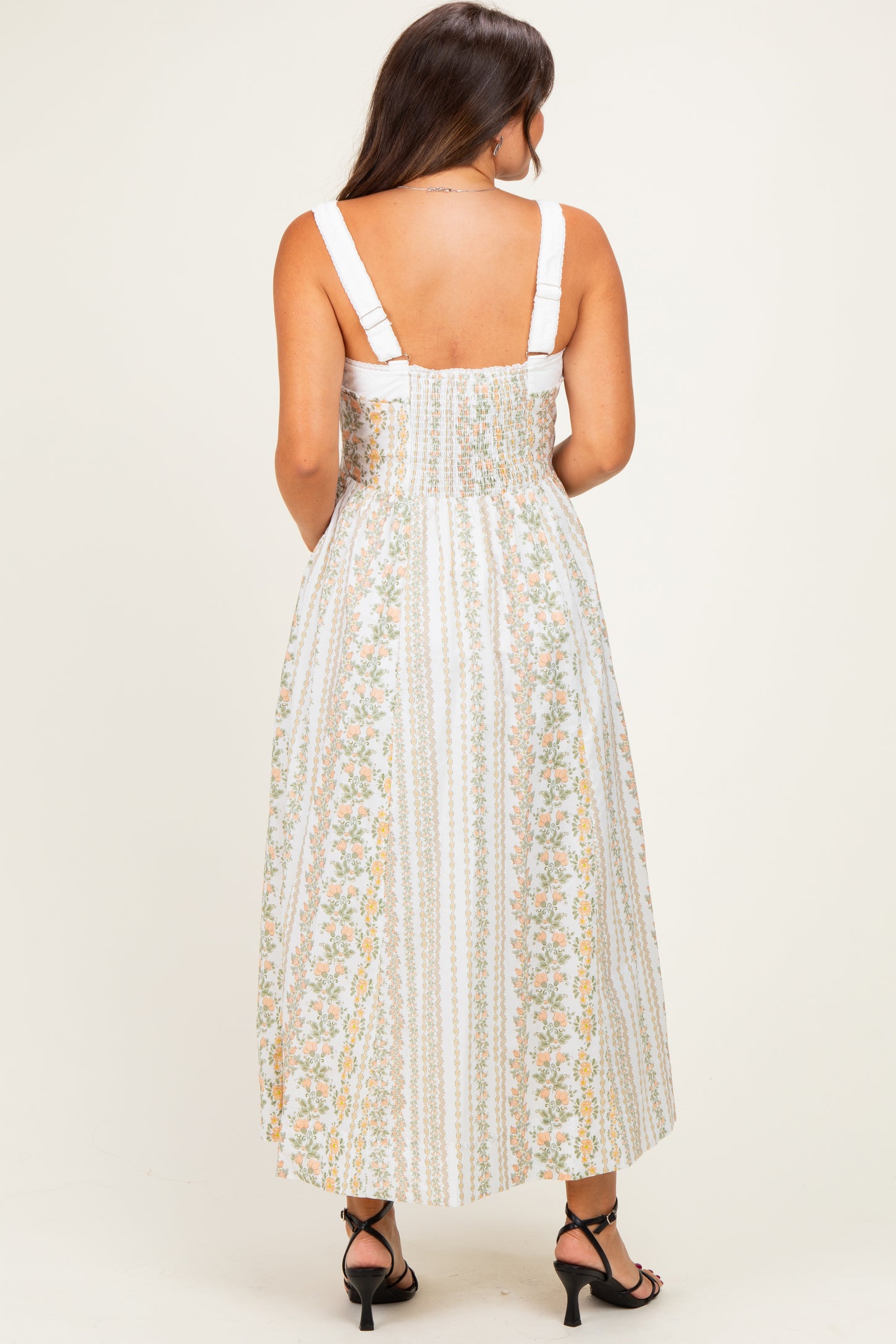 woman wearing a white floral maternity maxi dress with adjustable straps and a smocked back design