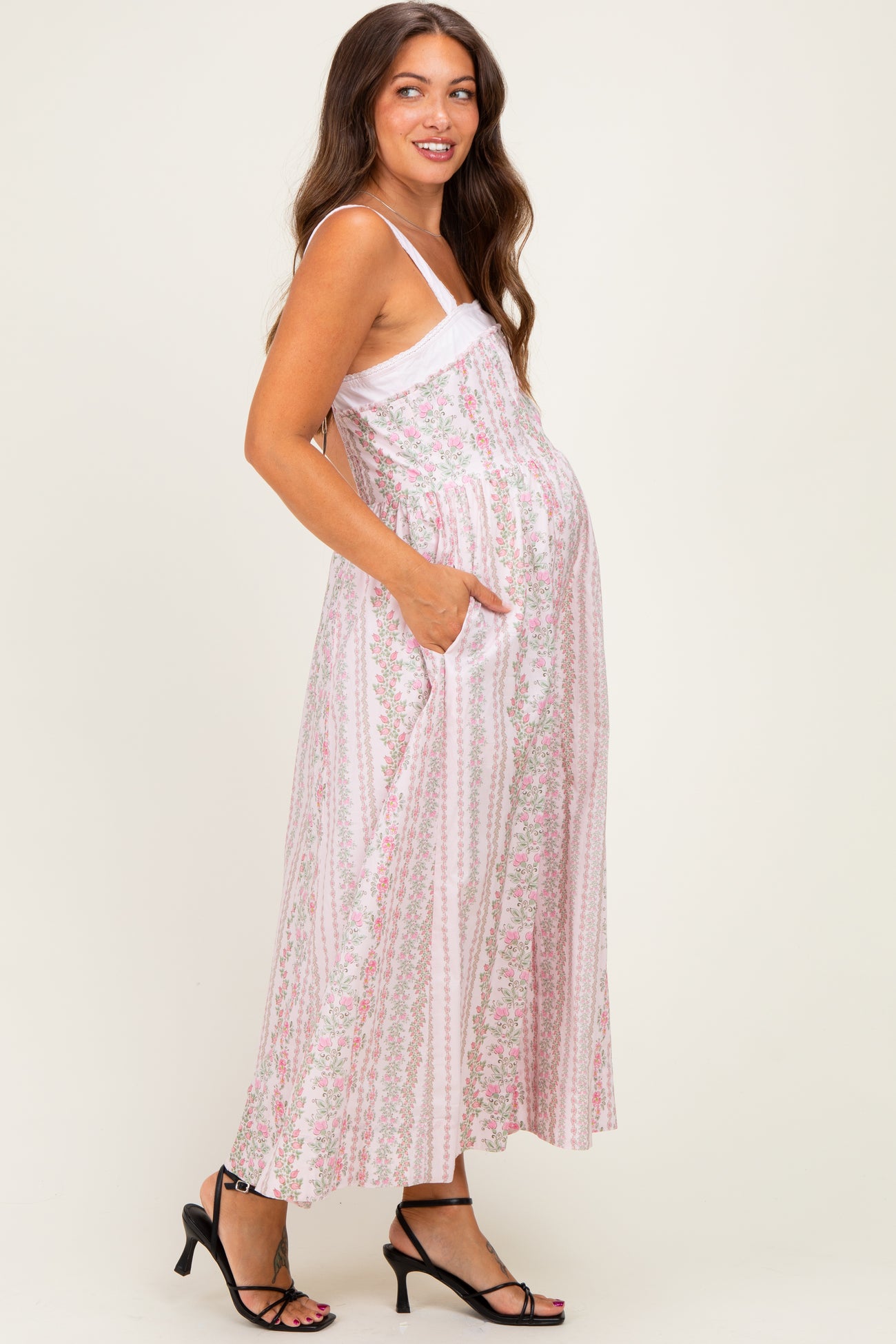 woman wearing a pink floral maternity maxi dress with pockets and a visible baby bump