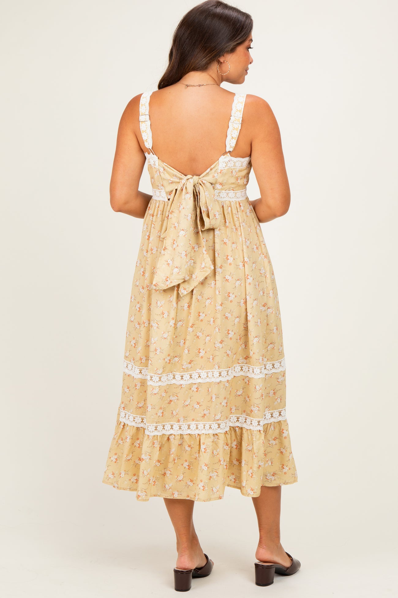 woman wearing a yellow floral maternity dress with lace details and a tie-back, showing a baby bump