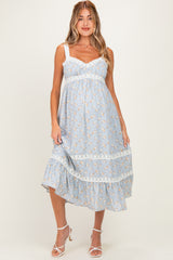 woman wearing a light blue floral maternity dress with lace detailing and a flowing skirt, showcasing her baby bump