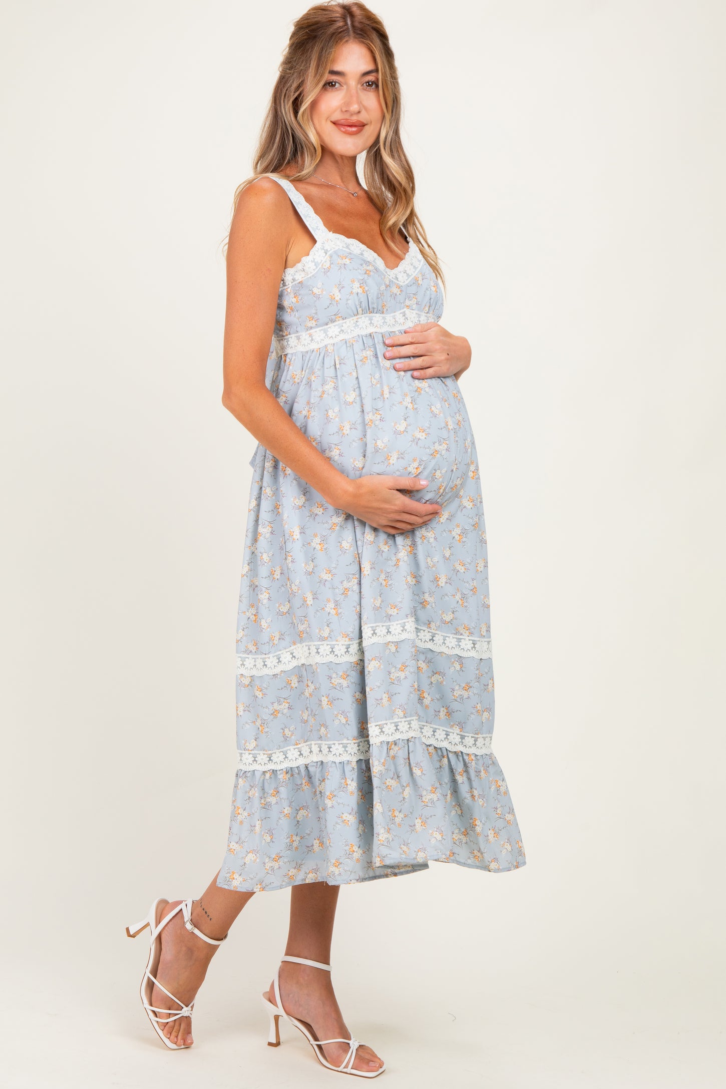woman wearing a light blue floral maternity dress with lace details, showing her baby bump while smiling