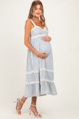 woman wearing a light blue floral maternity dress with lace details, showing her baby bump while smiling