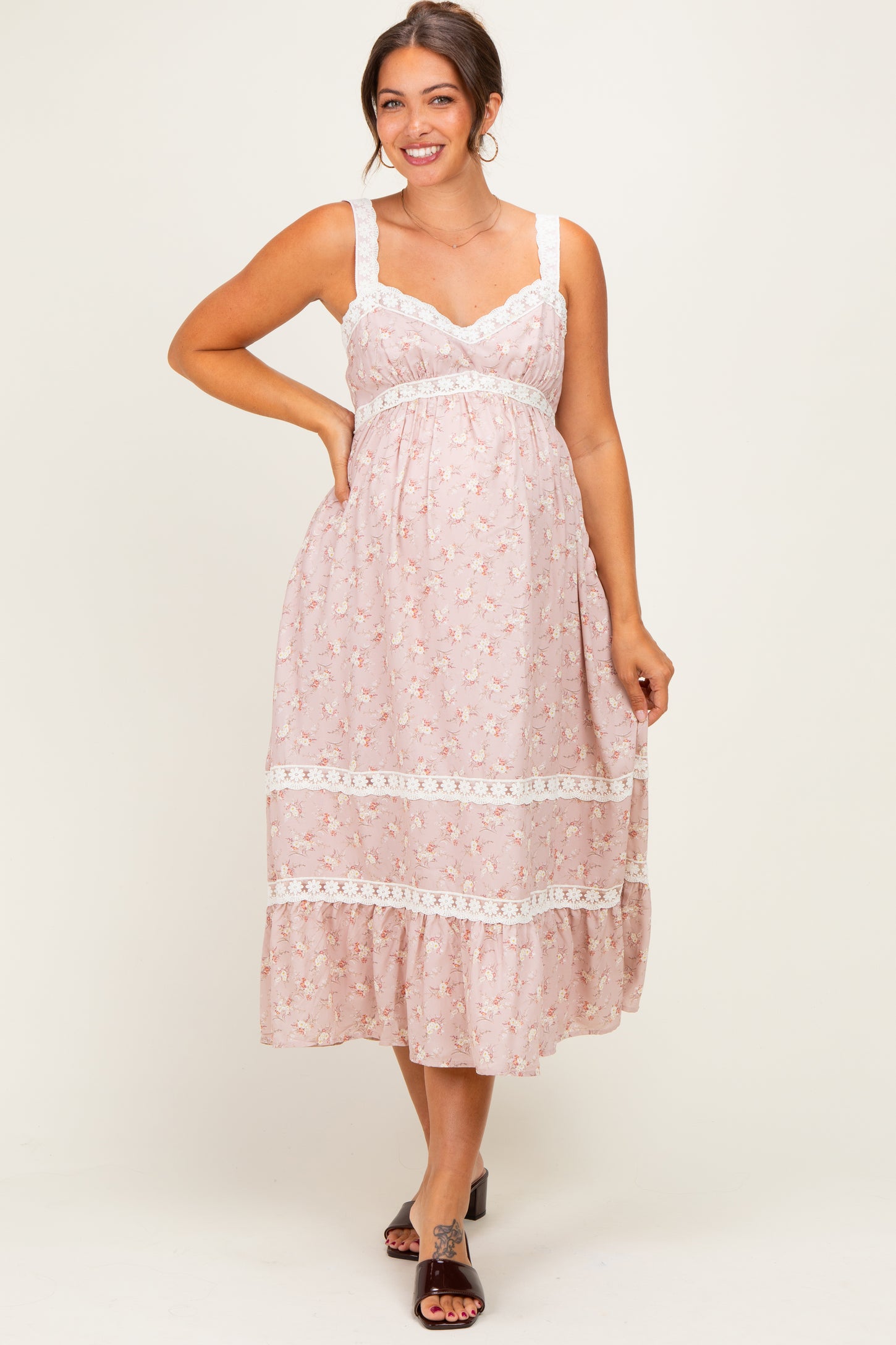 woman wearing a pink floral maternity dress with lace detailing and a flowing skirt, showing her baby bump
