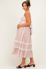 woman wearing a pink floral maternity dress with lace details and adjustable straps, holding her baby bump