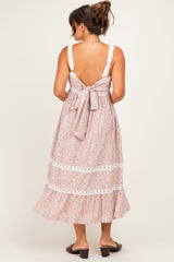 woman wearing a light pink maternity maxi dress with lace details and a tied back, showing a flowing skirt and no visible baby bump