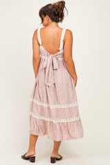 woman wearing a pink floral maternity dress with a tie-back detail and lace trim