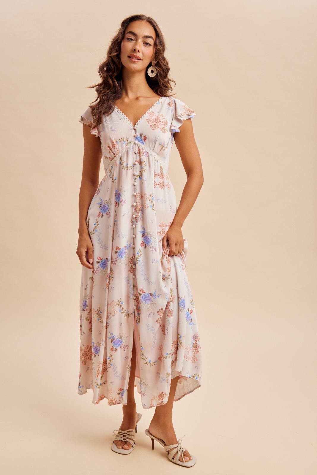 woman wearing a cream floral maxi dress with ruffle sleeves and a cinched waist