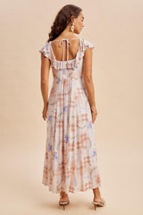 woman wearing a floral maxi dress with ruffled sleeves and an open back, standing against a neutral background