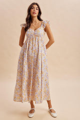 woman wearing a floral maxi dress with ruffled sleeves and a gathered bodice, standing with a neutral backdrop
